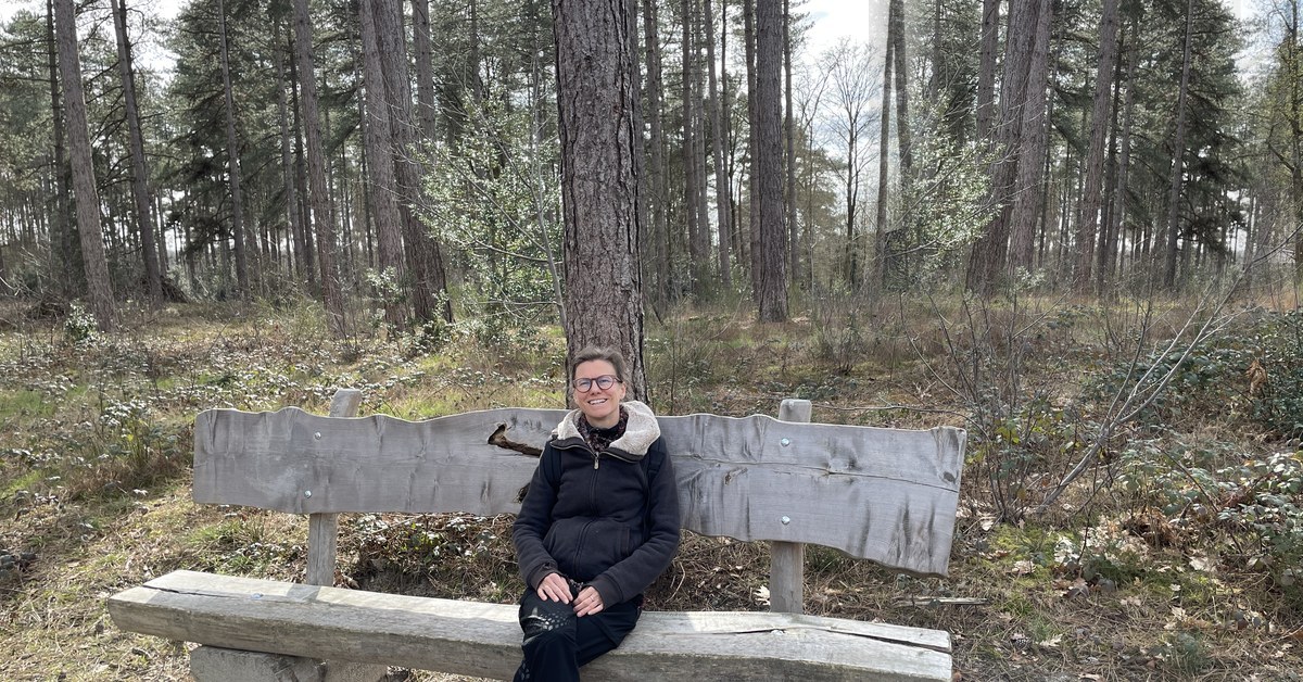 Elke Aerts van Centrum Nexus zittend op een houten bank in het bos — natuur en stilte als basis voor hypnomeditatie en de BONK-methode.